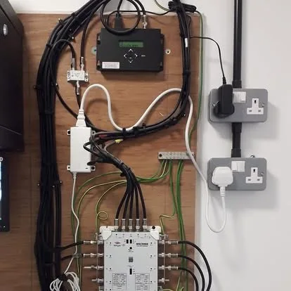 A communal distribution board with multiswitch, amplifier and labelled cable runs on a backboard.